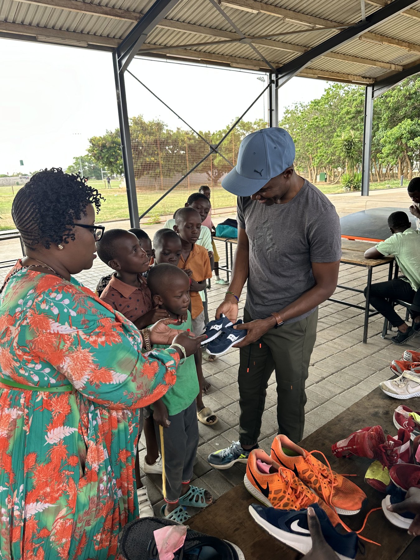 Prince Mumba handing a pair of running shoes to a child at a shoe donation event in Zambia