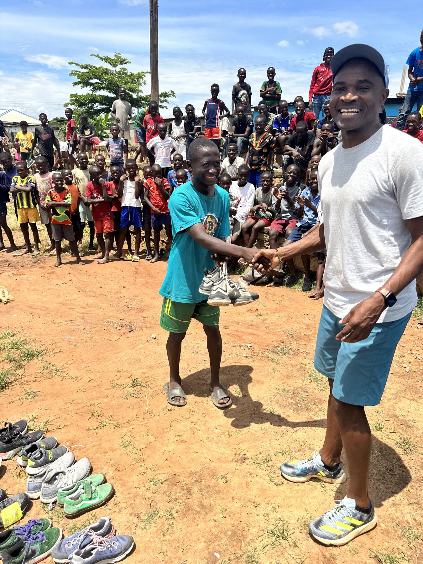 Prince Mumba shaking hands with a smiling boy holding his new running shoes in Zambia