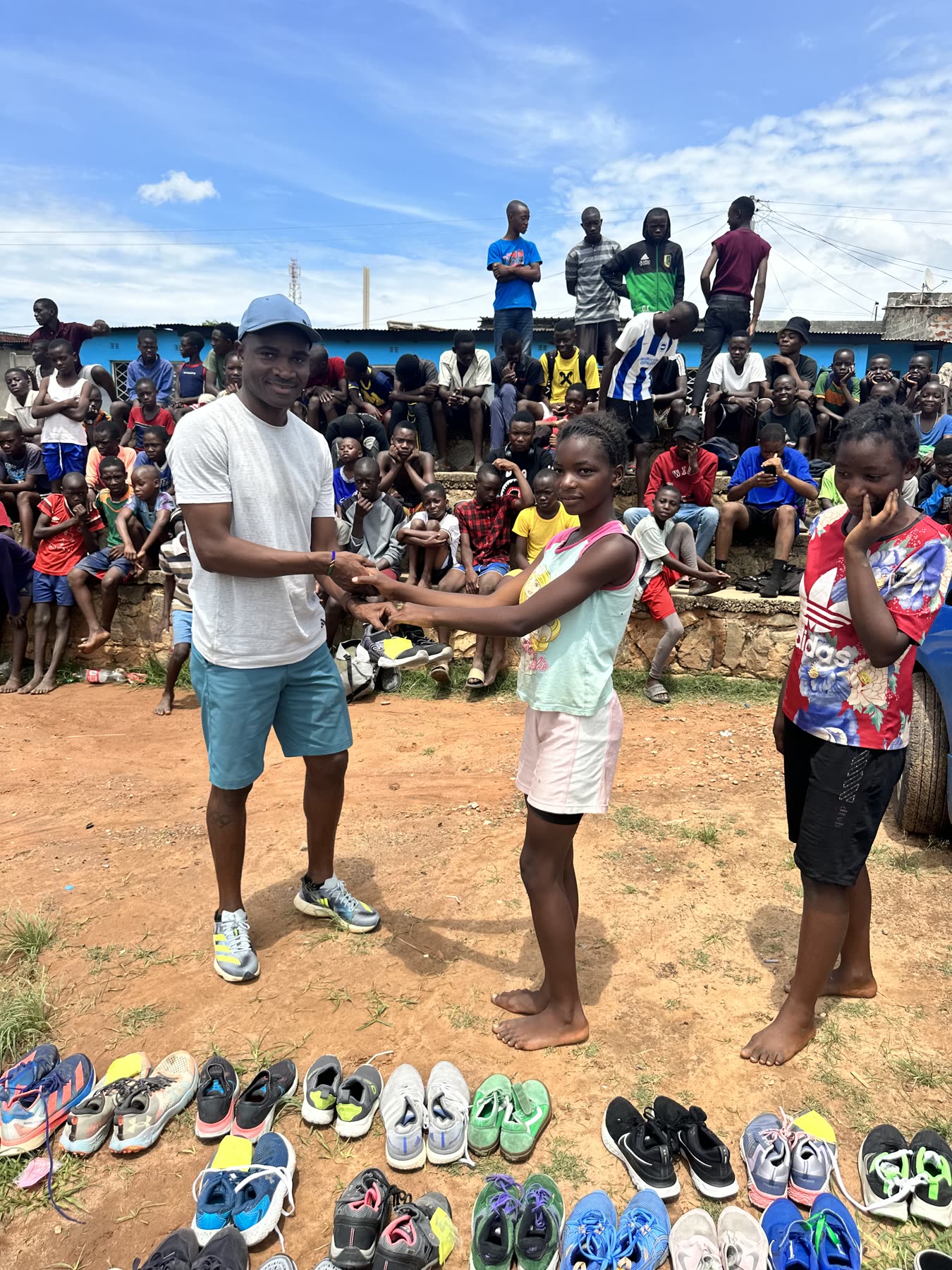 Prince Mumba handing a pair of donated running shoes to a young runner in Zambia